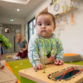 Tout-petit enfant de moins d'un an face à la caméra très joufflu et jouant sur une table d'éveil.
