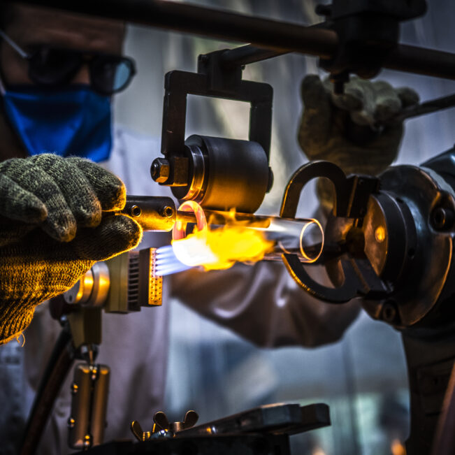 Industriel équipé de protections pour travailler le verre directement sur des flammes à l'aide d'un chalumeau.