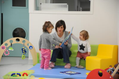 Deux petites filles en bas âge regardant un livre pour enfants avec une professionnelle de la crèche. - Agrandir l'image 3 sur 3, fenêtre modale