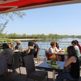 Plusieurs tables abritées en terrasse au bar-restaurant Le Louisabella situé face au Lac de Biron.