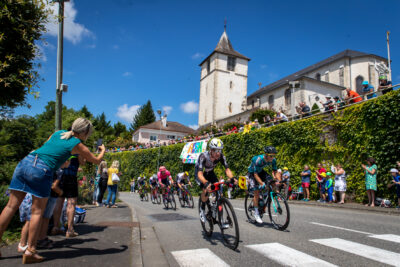 Vue du centre d'Arthez-de-Béarn avec l'église du village surplombant une route sur laquelle de nombreux cyclistes pédalent pour terminer premier, avec autour un public. - Agrandir l'image 3 sur 3, fenêtre modale