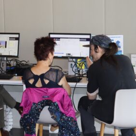 Un médiateurs des cyberbases est assis devant un ordinateur avec une dame demandant de l'aide pour se servir d'un ordinateur.