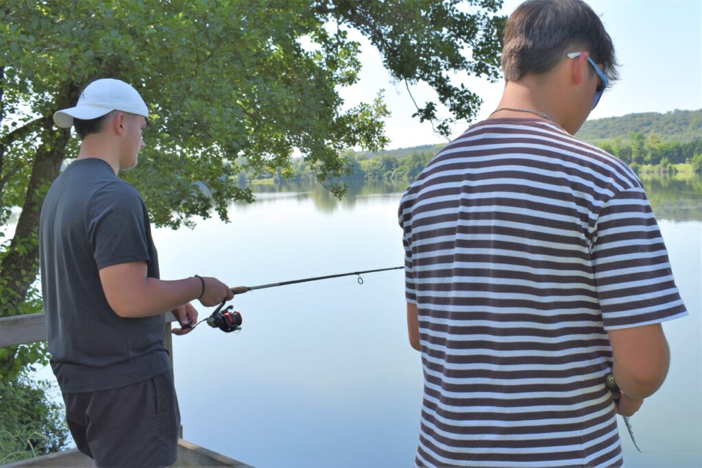 Deux adolescent pêchant côte à côte sous un arbre face au Lac de Biron. - Agrandir l'image, fenêtre modale