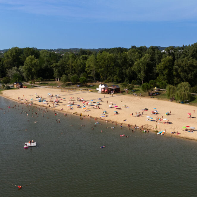 Vue du ciel de la plage de sable fin de la Base de loisirs et ses nombreux vacanciers, ainsi que du lac de Biron.