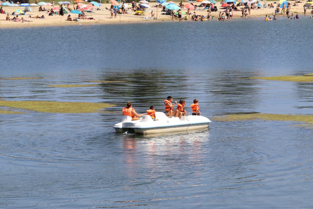 Groupe de vacanciers avec des gilets de sauvetage profitant d'un pédalo blanc de location sur le lac près de la plage. - Agrandir l'image, fenêtre modale