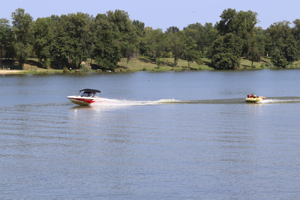 Deux personnes sur une bouée tractée par un petit bateau à moteur sur le lac de Biron. - Agrandir l'image, fenêtre modale