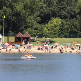 Vacanciers sur la plage de sable fin bordant le Lac de Biron pendant que d'autres font du pédalo