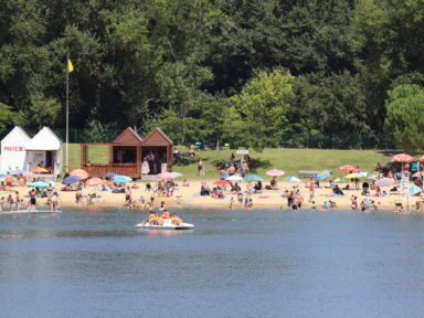 Vacanciers sur la plage de sable fin bordant le Lac de Biron pendant que d'autres font du pédalo