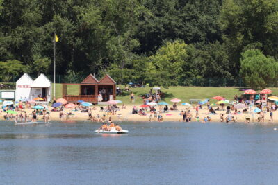 Vacanciers sur la plage de sable fin bordant le Lac de Biron pendant que d'autres font du pédalo - Agrandir l'image 1 sur 5, fenêtre modale