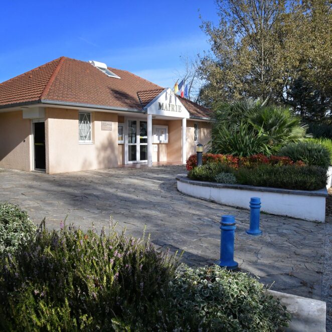 vue sur le bâtiment de la mairie au sommet d'une légère côte. L'entrée du bâtiment se fait à travers un petit porche et des portes vitrées.