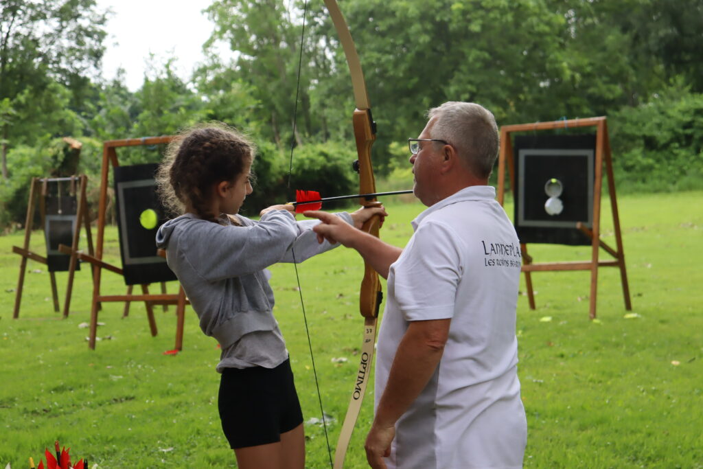 Jeune adolescente s'essayant au tir à l'arc sous les conseils avisés d'un bénévole de l'association. - Agrandir l'image, fenêtre modale