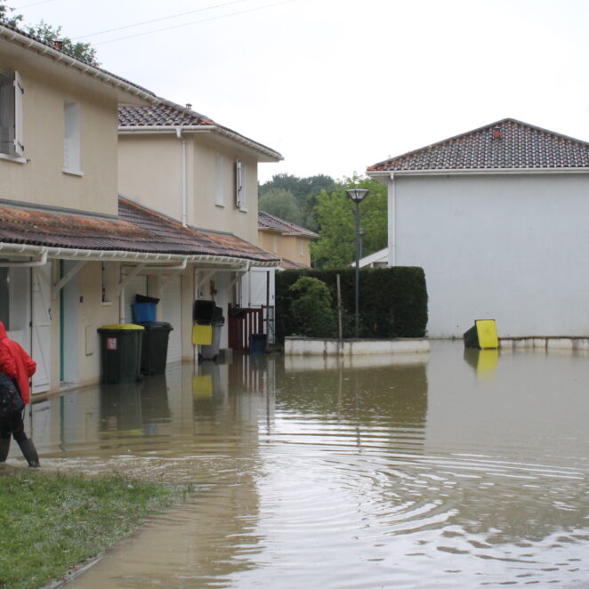 Personnes avec des bottes, passant près d'une résidence avec un début d'inondation.