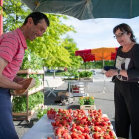 Une habitante du territoire face à un commerçant pour lui acheter des barquettes de fraises locale sur un marché.