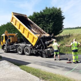 Trois agents du service voirie qui refont le bitume d'une petite route de campagne.