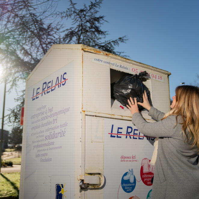 Jeune femme déposant dans un sac fermé, des textiles qu'elle n'utilise plus dans une borne dédiée.