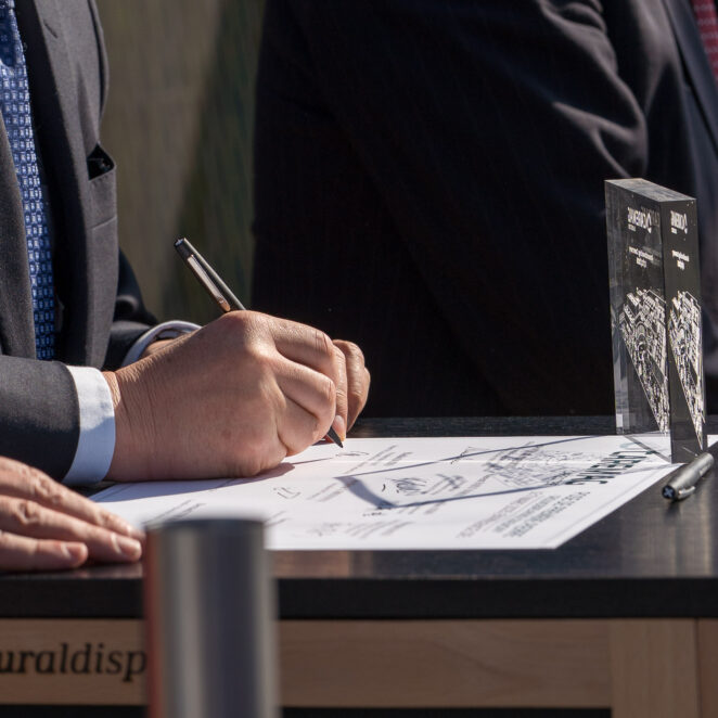 Homme signant un contrat sur table avec un trophée transparent devant lui.