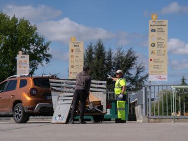 Un agent de déchetterie montrant du doigt à un habitant l'emplacement de la benne dans laquelle il doit jeter le contenu de sa remorque.