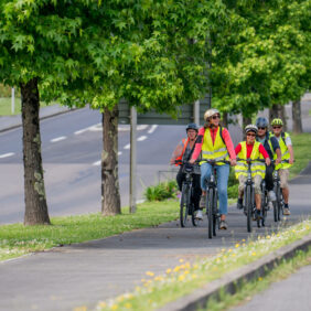 Groupe de cyclistes avec casque et gilets jaunes se promenant sur une piste cyclable sécurisée en plein cœur d'une commune et à côté d'une route.