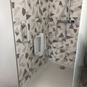Cabine de douche initialement conçue pour une personne sans problématiques physique, finalement adaptée aux personnes à mobilité réduite avec une barre de soutien et un siège afin que l'occupant du logement n'aie pas besoin de changer de logement.
