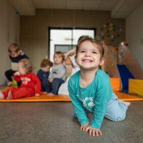 Petite fille de moins de quatre an souriant à la caméra assise sur le sol de l'une des crèches du territoire.