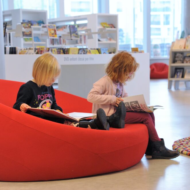Deux enfants en bas âge lisant des BD sur des poufs à la médiathèque du MIX.