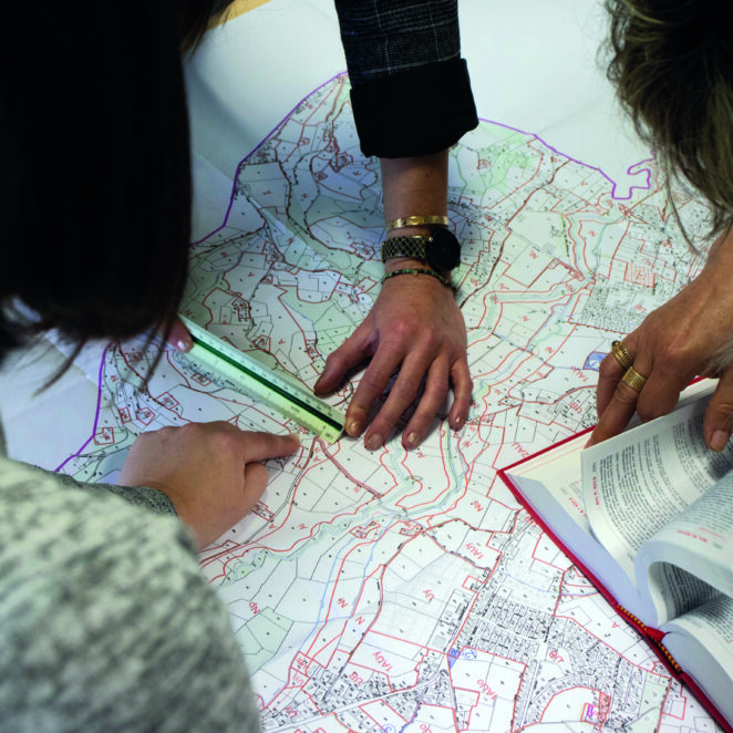 Trois agents du service urbanisme penchés sur une carte avec le code de l'urbanisme pour effectuer leur travail.