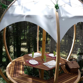 Hébergement insolite avec une table et des assiettes dans une forme circulaire, suspendu au dessus du vide et protégé de filets en pleine forêt.