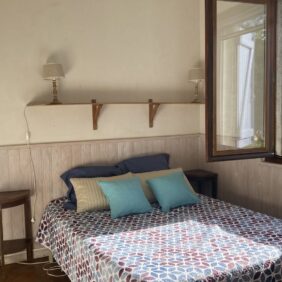 Chambre d'hôtes avec un lit double fait et une fenêtre ouverture avec vue sur les champs et les montagnes.