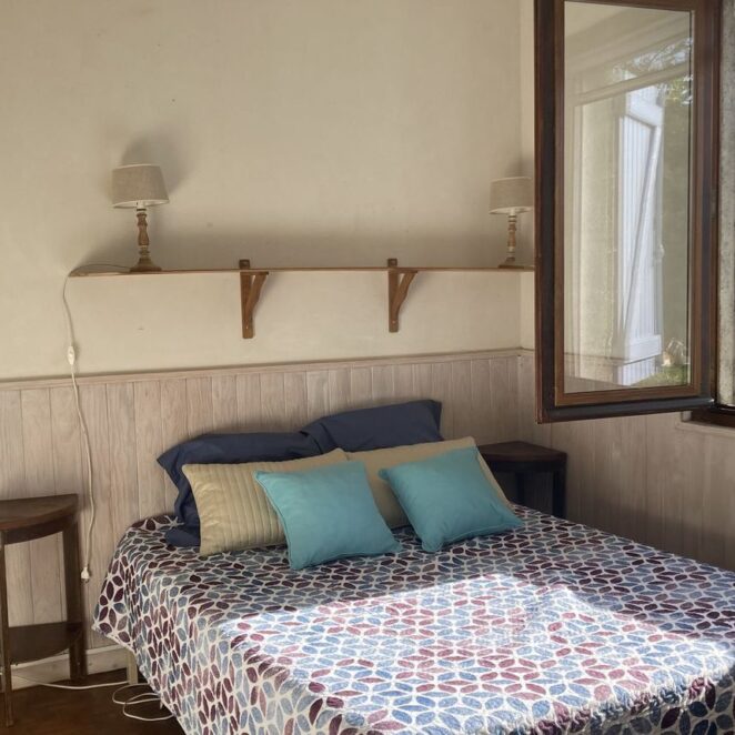 Chambre d'hôtes avec un lit double fait et une fenêtre ouverture avec vue sur les champs et les montagnes.