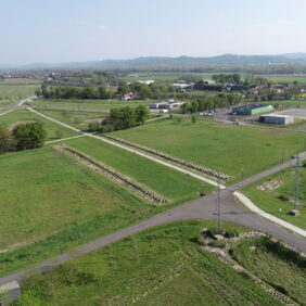 Prise de vue du ciel de terrains nus et de bâtiments hébergeant des entreprises sur le territoire, avec en fond des forêts et les montagnes.