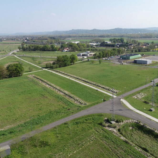 Prise de vue du ciel de terrains nus et de bâtiments hébergeant des entreprises sur le territoire, avec en fond des forêts et les montagnes.
