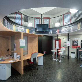 Hall avec le plafond ouvert sur les portes des bureaux du premier étage, et au rez-de-chaussée, un espace coworking avec 4 bureaux, des mange-debout et des machines à café.