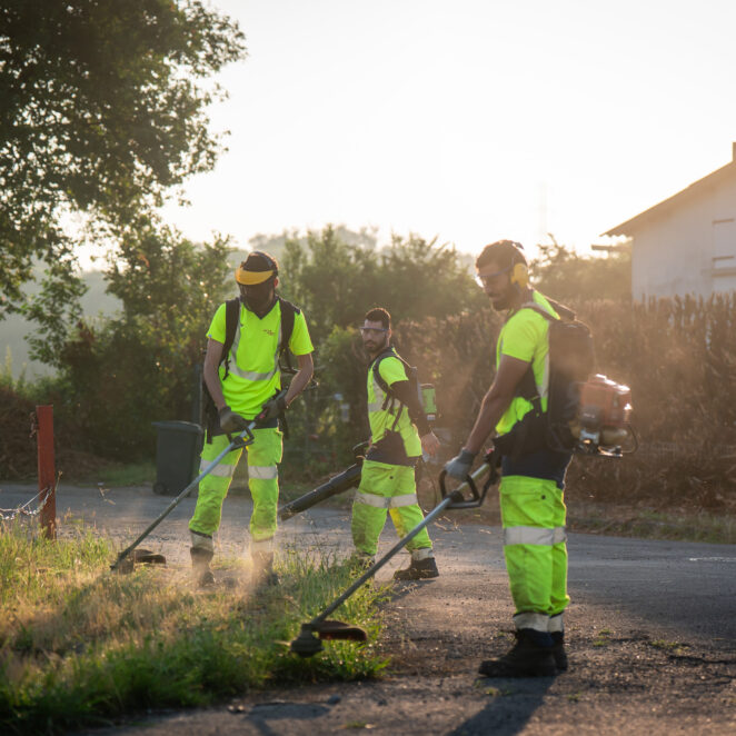 Trois agents en tenue avec visière de protection et casques sur les oreilles, ont dans leur main des rotofiles afin de couper l'herbe aux abords des talus.
