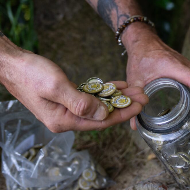 Personne avec des pin's en main sortis d'une bouteille au pied d'un arbre que l'on récupère une fois que l'on a trouvé toutes les énigmes du parcours Terra Aventura.