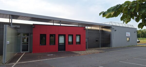 Rouge et grise, la médiathèque de Monein est un grand bâtiment de plein pied entouré d'un parking