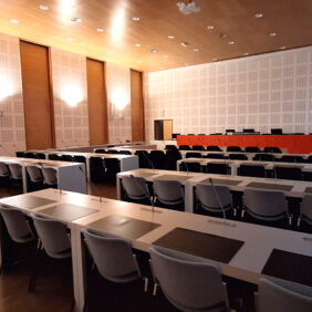Grande salle dans laquelle 4 rangés de tables sont alignées face à une rangée de table rouge surélevée