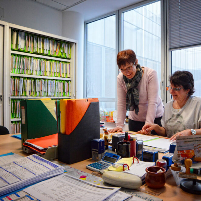 Deux femmes travaillant dans un bureau au milieu de nombreux documents administratifs.