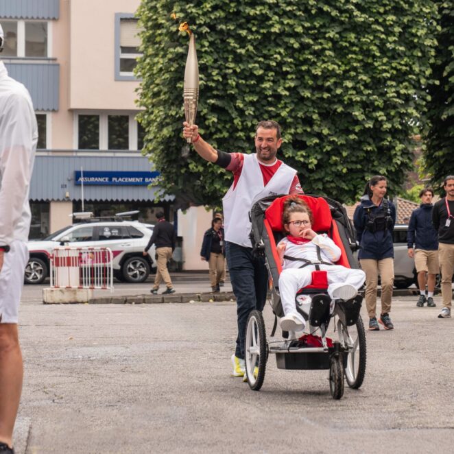 Une personne tenant la flamme olympique poussant une poussette adaptée au handicap d'une petite fille de 10 ans.