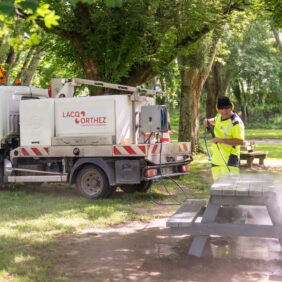 Agent avec une tenue jaune réfléchissante, nettoyant au karsher une table de pique-nique.