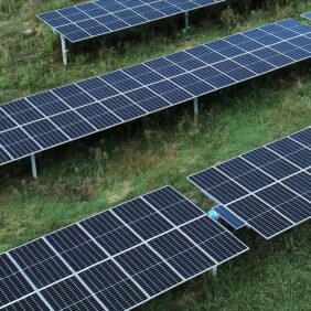 Trois rangées de panneaux solaires vue en diagonale dans une prairie.