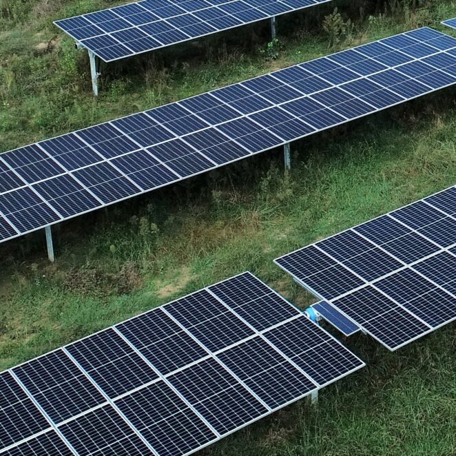 Trois rangées de panneaux solaires vue en diagonale dans une prairie.