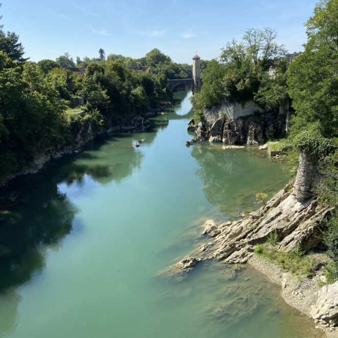 Vue du Gave de Pau qui passe sous le Pont-vieux d'Orthez. Le cours d'eau est à la verticale face à nous, et de part et d'autres se trouve des espaces naturels et un peu de roche.