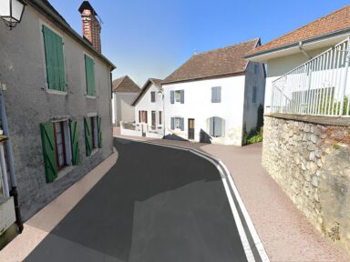 Vue après travaux montrant une route en vertical face à nous avec des maisons de part et d'autre, un revêtement neuf et des trottoirs aux couleurs clairs et assez larges pour les fauteuils roulant.