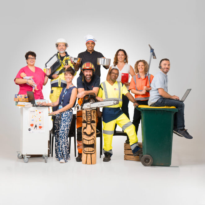 9 agents de la collectivité issus de métiers différents, posent en tenue de travail sur un fond uni. De gauche à droite, on voit une assistante maternelle avec un poupon dans la main gauche et un biberon dans la main droite, à côté un agent des services techniques avec des machines dans les mains qui ressemble à une tablette, à côté un cuisinier avec sa toque et deux récipient un dans chaque main, à côté une femme des services administratifs en tenue simple mais tenant en main le code de l'urbanisme, à côté une femme des services techniques avec une pioche dans les mains, à côté un agent d'accueil avec un micro-casque et un ordinateur sur les genoux, il est assis sur une poubelle au couvercle jaune. A gauche de la poubelle se tient un agent du service déchets tenant la poubelle, à sa gauche un agent des services techniques accoudé sur un totem de bois et tenant une tronçonneuse, et à sa gauche, une médiathécaire habillée décontracté avec un ordinateur devant elle et un support roulant avec une affiche du centre culturel Le MIX accroché dessus et transportant divers bouquins.