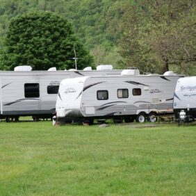 Terrain de verdure aux abords d'une forêt verdoyante sur lequel plusieurs caravanes double essieu sont arrêtées.