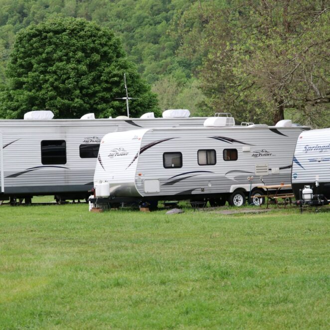 Terrain de verdure aux abords d'une forêt verdoyante sur lequel plusieurs caravanes double essieu sont arrêtées.