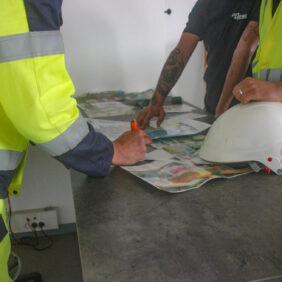 Des agents du BTP et un chef d'entreprise regardent ensemble les plans d'une future extension des bâtiments de l'entreprise.