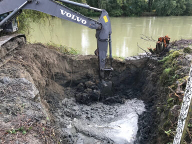 Tractopelle creusant un nouveau bras à la source d'eau que l'on voit en arrière plan afin que l'eau puisse s'écouler à l'intérieur et disposer de plus d'espace.