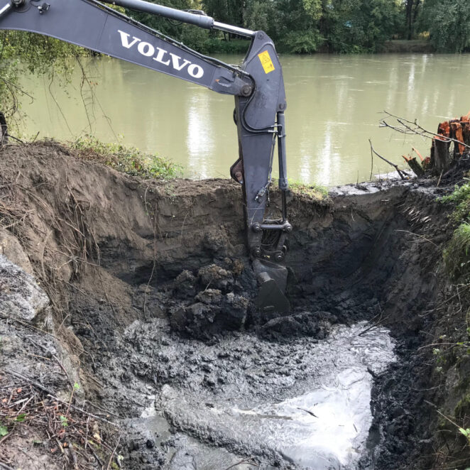 Tractopelle creusant un nouveau bras à la source d'eau que l'on voit en arrière plan afin que l'eau puisse s'écouler à l'intérieur et disposer de plus d'espace.
